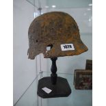 Military helmet bearing Nazi insignia on purpose built wooden stand Heavy rusting and deterioration