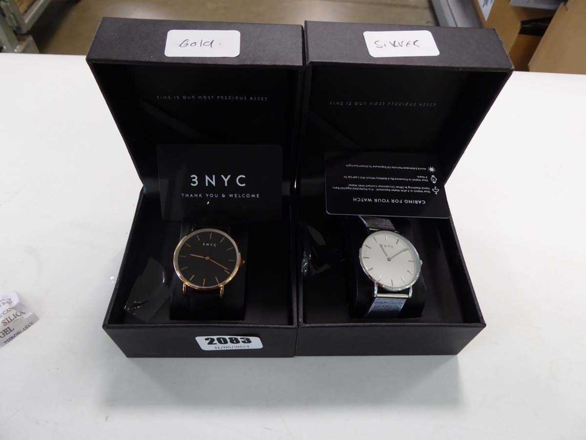 2x 3 NYC watches, 1 with gold strap and black face and 1 with silver strap and white face