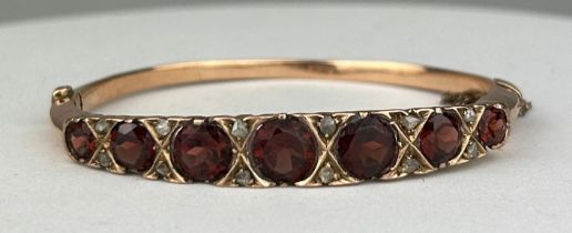 A VICTORIAN 9CT GOLD BANGLE SET WITH SEVEN RED GARNETS OF GRADUATING SIZE, 6.5cm in diameter x 6cm