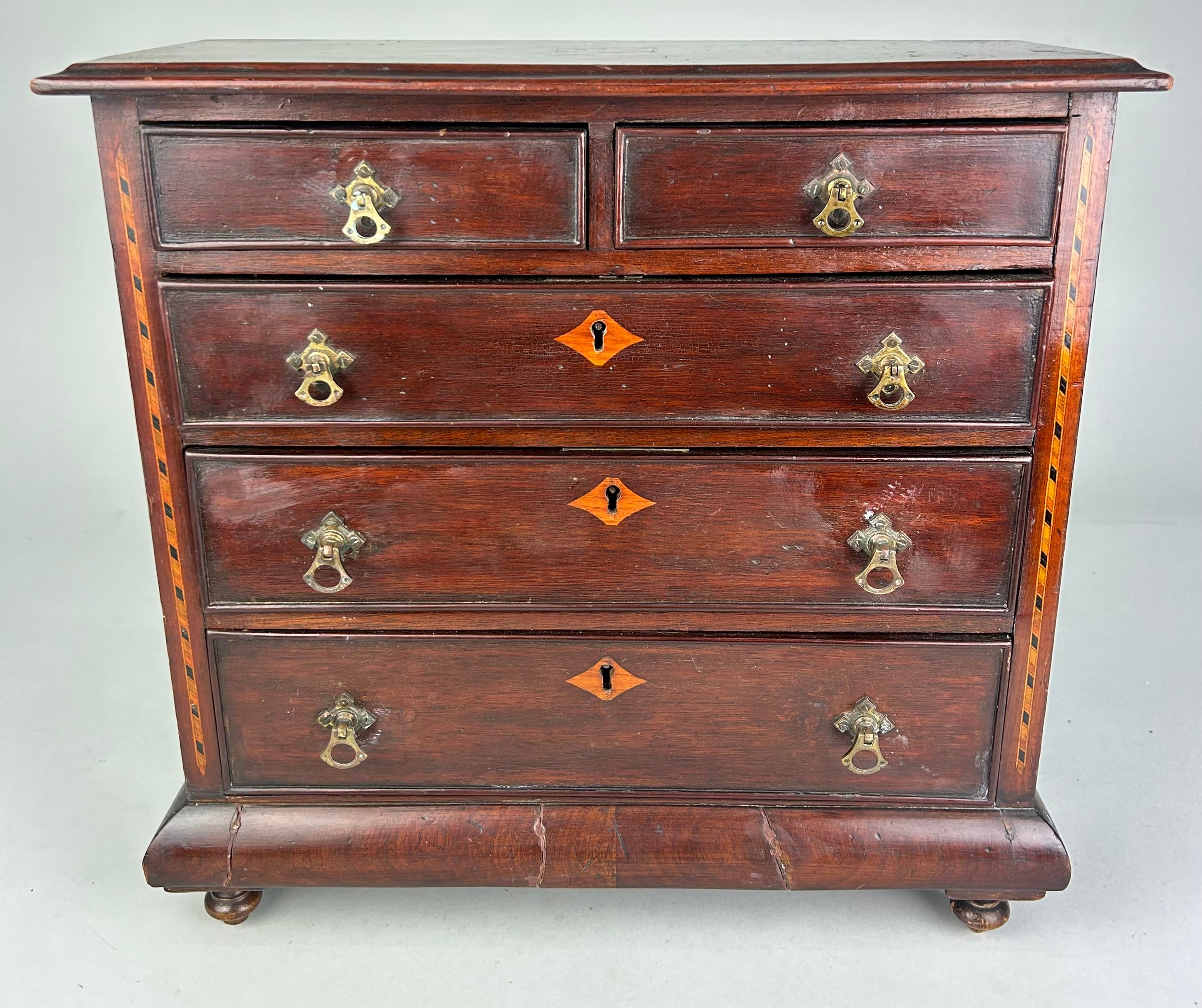 AN EARLY 19TH CENTURY APPRENTICE CHEST OF DRAWERS, With parquetry inlay raised on turned feet.
