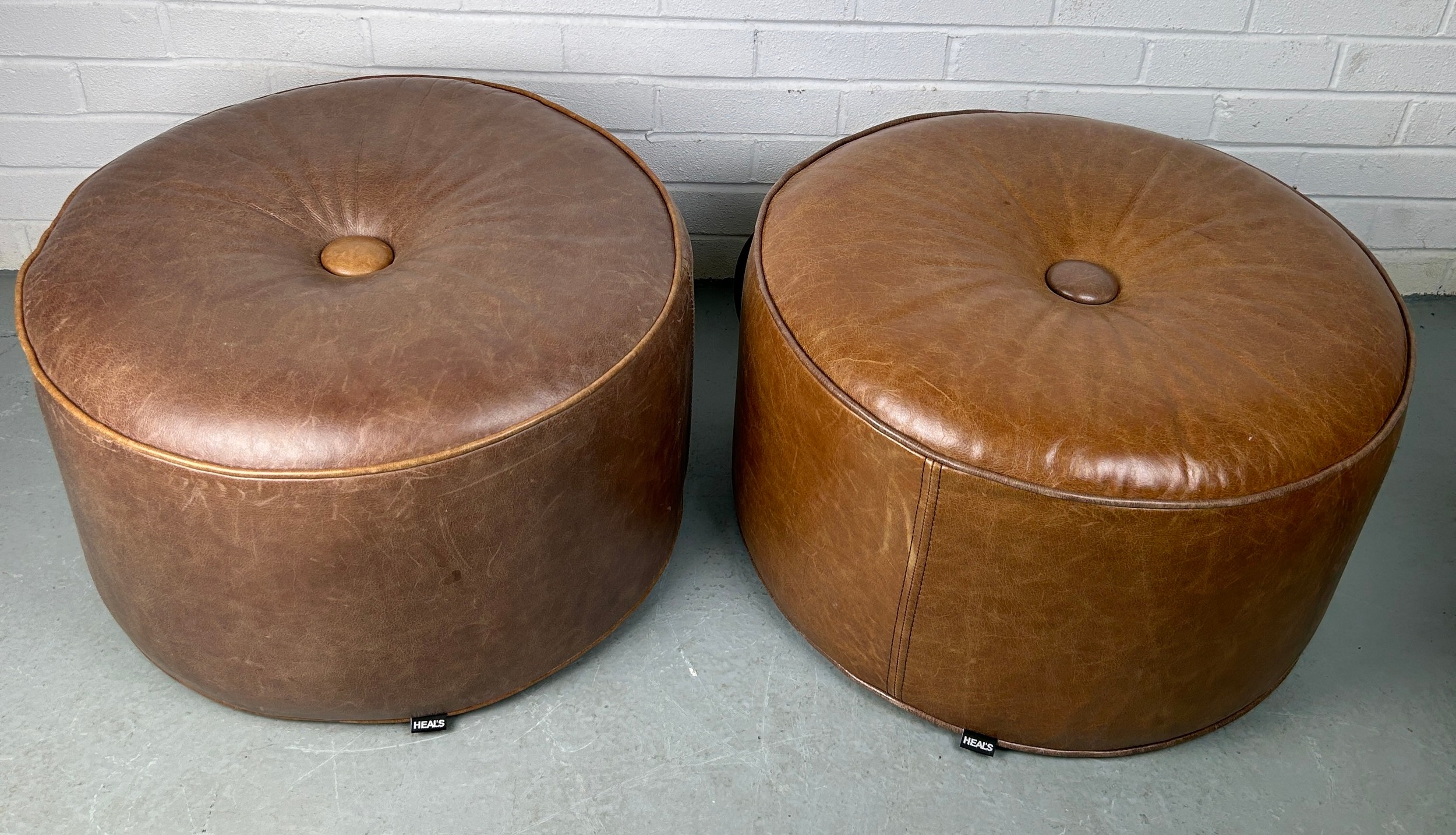 A PAIR OF HEALS CIRCULAR STOOLS OR POUFFES UPHOLSTERED IN TAN LEATHER, 60cm x 35cm each.