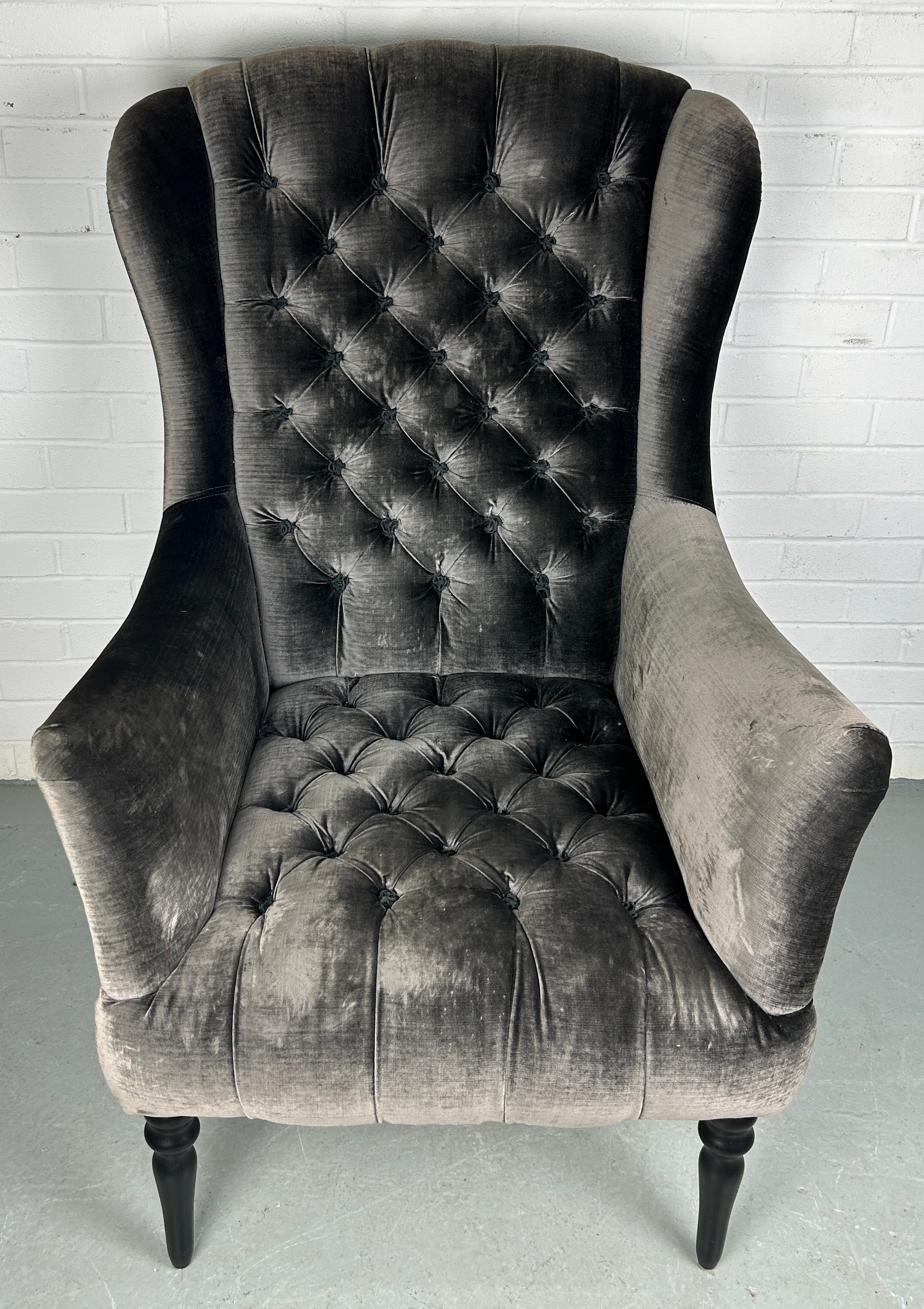 JOHN SANKEY: A WINGBACK ARMCHAIR ON FOUR EBONISED LEGS UPHOLSTERED IN BUTTON BACK VELVET FABRIC,