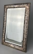 A FOREIGN REPOUSSE SILVER PICTURE FRAME MIRROR DECORATED WITH FLOWERS, 36cm x 23cm