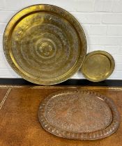 A LARGE ISLAMIC BRASS DISH ALONG WITH A SMALLER EXAMPLE AND A COPPER DISH, Largest 59cm D