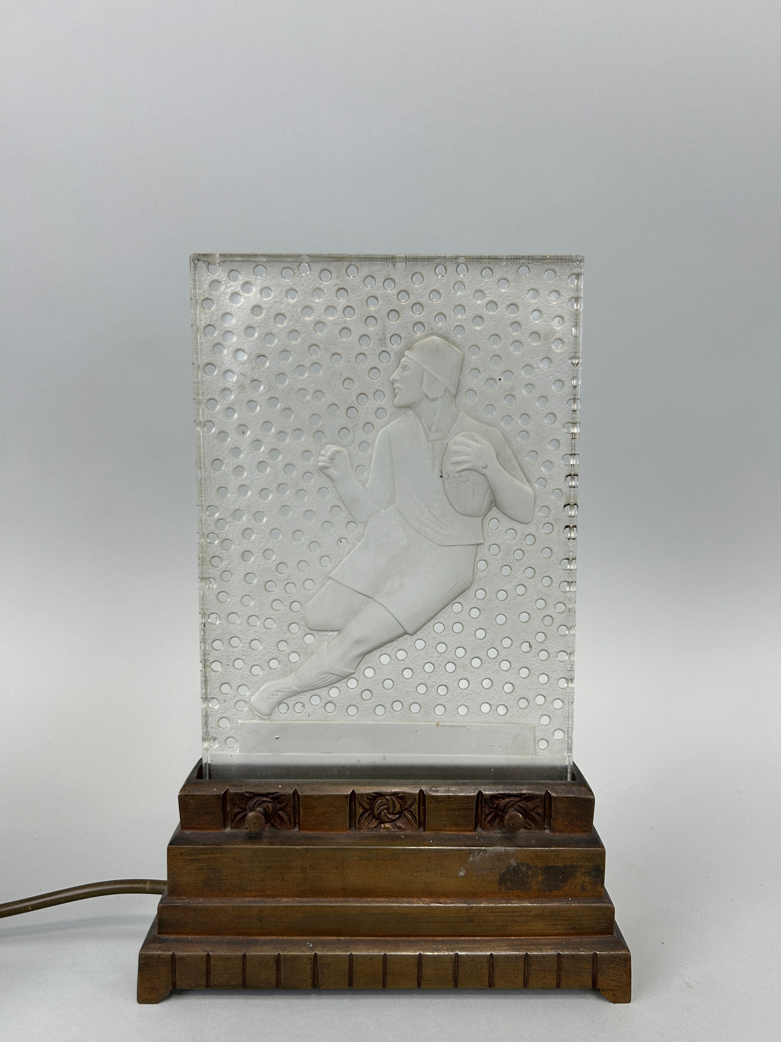 AN ART DECO VERLYS PRESSED GLASS LIGHT ON STAND IN THE FORM OF A RUGBY PLAYER, 30cm x 19cm