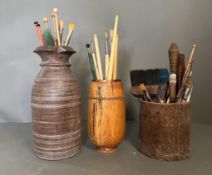 Three wooden pots containing a selection of vintage paint brushes