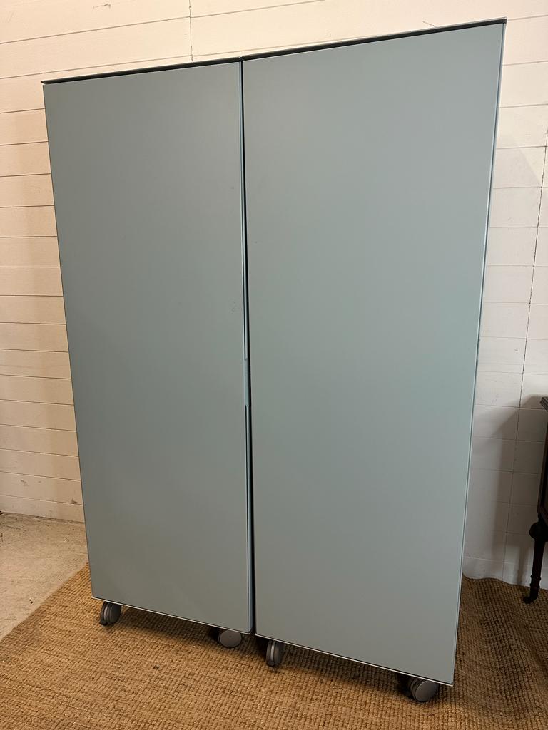 Two contemporary pale blue wardrobes on castor, one opening to reveal hanging rail and three shelves