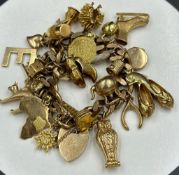 A 9ct gold charm bracelet with a wide and varied selection of charms and a heart shaped fastener.(