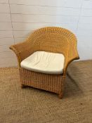 A wicker arm chair with white upholstered seat cushion
