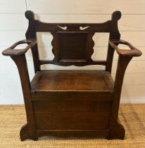 An oak Arts and Crafts hall stand bench with hinged lid to reveal storage and a carved back