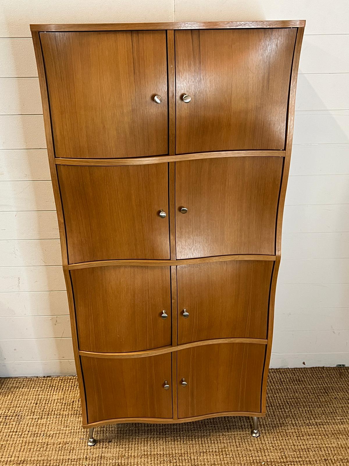 A contemporary wave front cabinet with eight compartments on chrome legs (74cm x 38cm x 155cm)