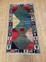 A hand knotted nomad rug in greens, reds and blues 153cm x 80cm
