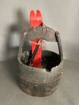 A wooden well bucket with metal banding along with wooden decorative skis glued in places