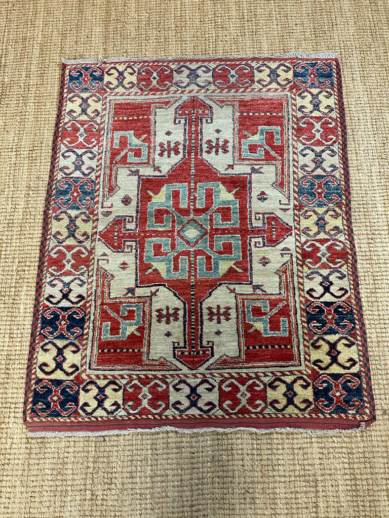 A red ground rug with a repeating Aztec pattern 123cm x 100cm