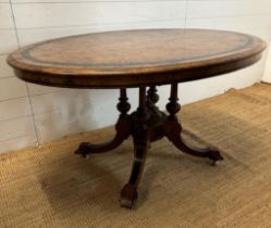 An oval walnut centre table with ebonised inlay and pierced floral detail, on four splayed legs with