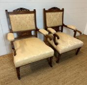 A pair of inlaid and carved open arm chairs on turned legs and castors, upholstered in a beige