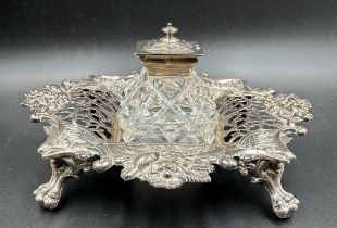 A Victorian cut glass and silver topped inkwell on a pierced silver stand with foliate decoration,