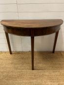 A Demi Lune mahogany table on tapering legs (H74cm W108cm D51cm)