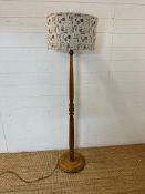 An oak turned floor standing lamp with a marine themed shade in blue and white