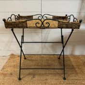 A wrought iron folding butlers tray with a wicker top and scrolling sides (H60cm W56cm D40cm)