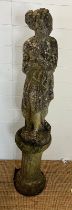 A weathered cast stone statue of a maiden with her arms clasped on a fluted circular base (H83cm