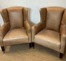 A pair of wing back tan leather arm chairs with brass castors