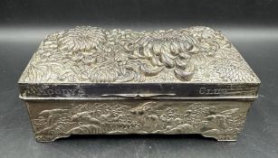 A hammered white metal cigarette box with floral motif, inscribed "Moodys Club" to the front and