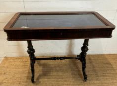 A glass topped bijouterie table on carved splayed legs with turned central stretcher. 100x54