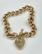 A curb link yellow 9ct gold bracelet with heart shaped fastener and safety chain