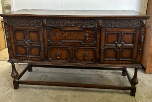 An oak dresser base with two central drawers flanked by two cupboards with carved fronts and