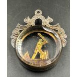 A silver and glass fob featuring a cricketer in action