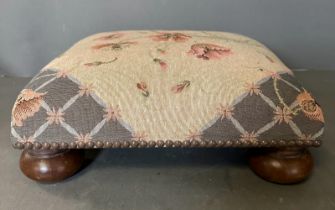 A floral upholstered and studded footstool on bun feet