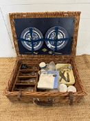 A wicker picnic basket comprising of blue and white plates, cutlery, thermos and plastic glasses