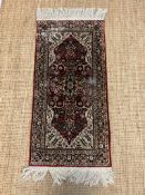 A silk runner rug with red grounds and a scrolling and floral design to centre