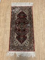 A silk runner rug with red grounds and a scrolling and floral design to centre
