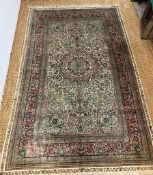 A silk and wool carpet/rug with floral border of reds and greens and rectangular centre panel of