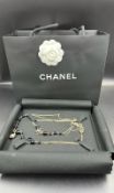 A Chanel long fashion necklace, black and gold themed, boxed with bag.