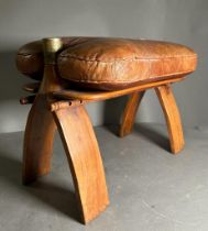 A middle Eastern camel stool with brown leather seat on a hardwood and brass frame
