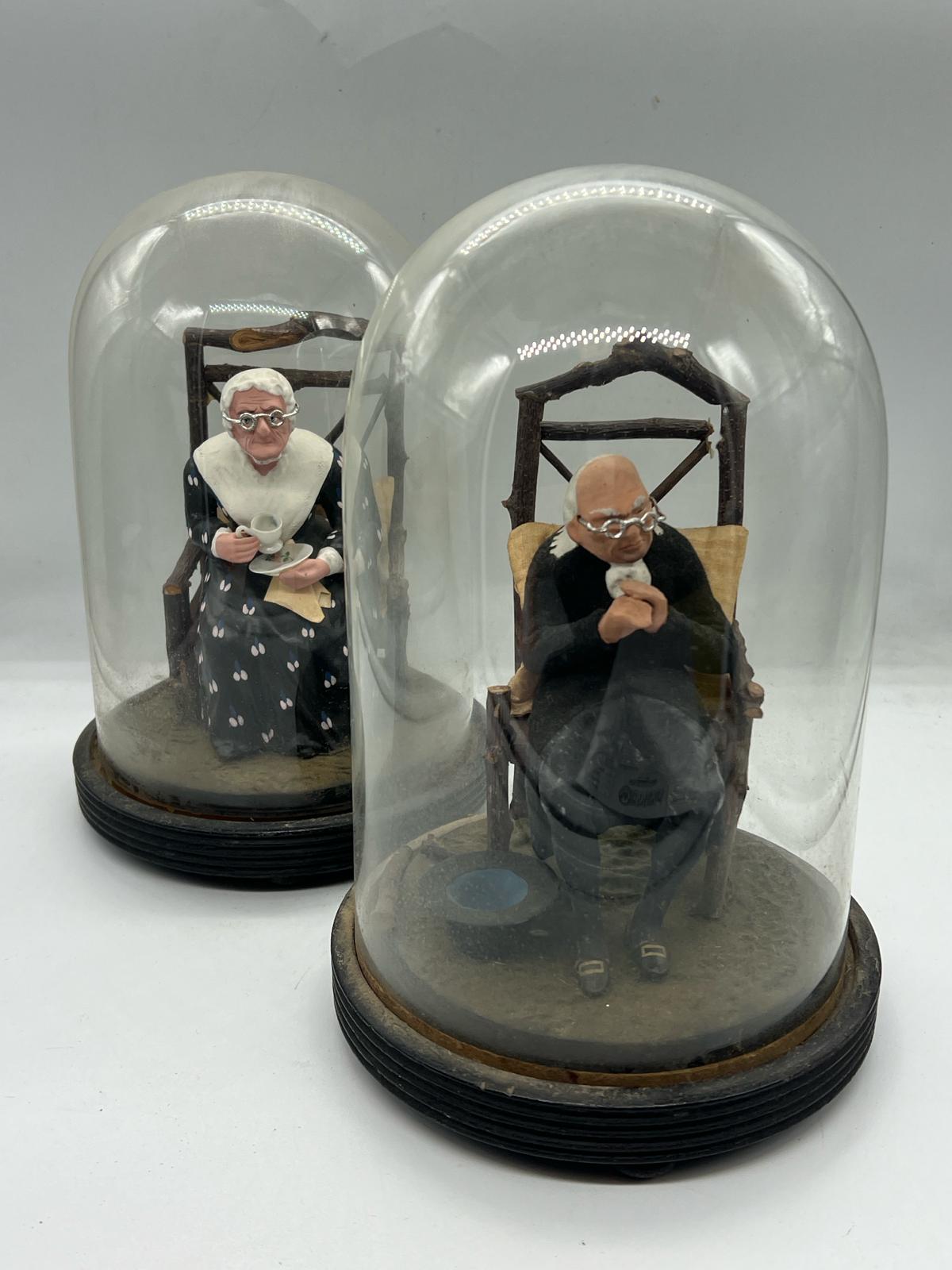 A pair of papier mache lady and gentleman seated figures under glass domes and linths (H23cm)