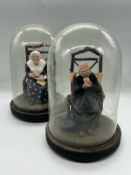 A pair of papier mache lady and gentleman seated figures under glass domes and linths (H23cm)