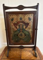 An Art Deco style mahogany fire screen with a peacock and gold detailed front panel on splayed feet