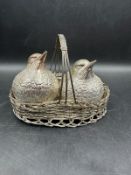 A white metal salt and pepper in the form of two chickens in a white metal basket