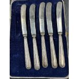 An incomplete set of five silver handled butter knives, cased.