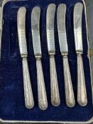 An incomplete set of five silver handled butter knives, cased.