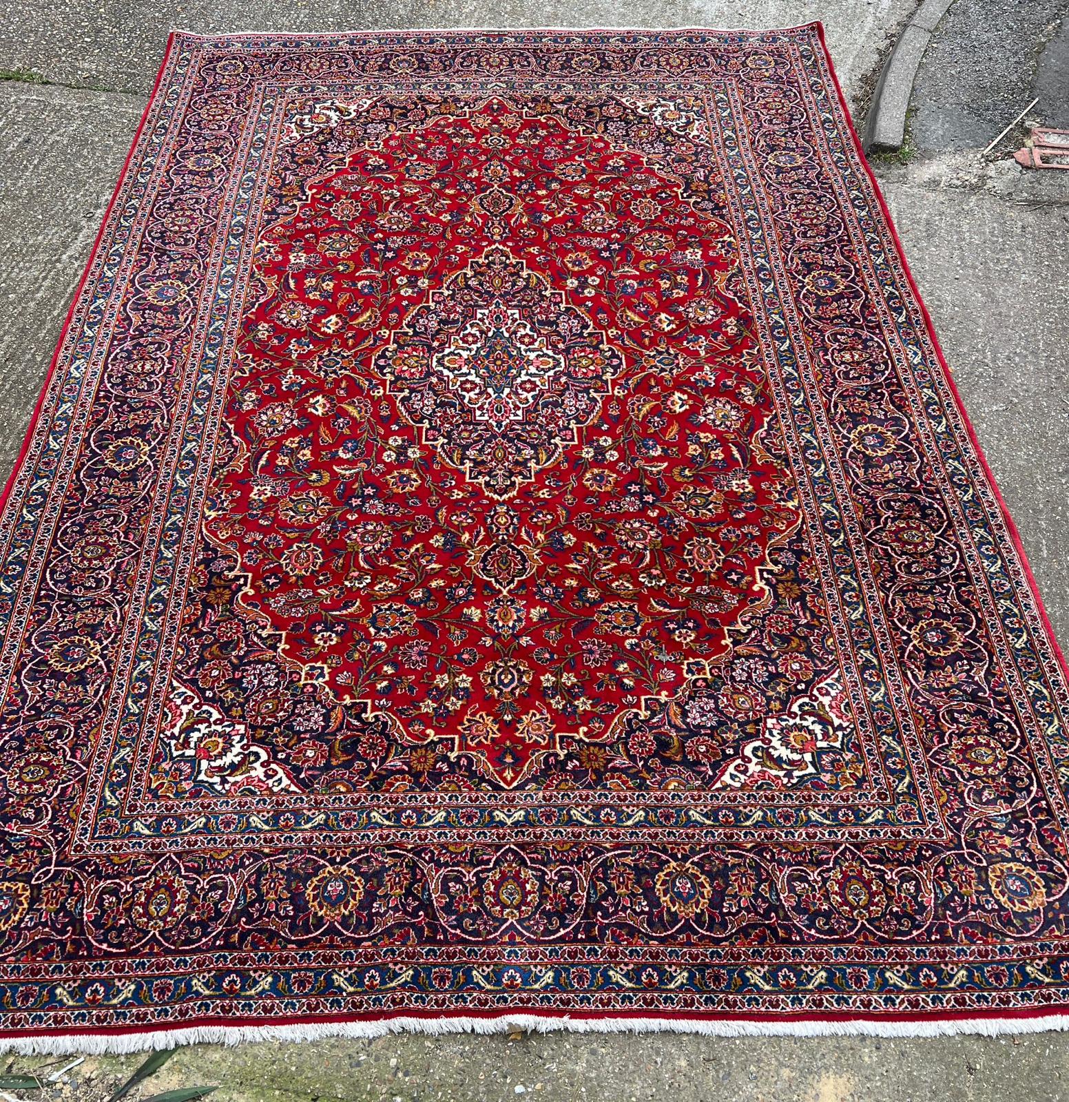 A hand knotted wool Kashan rug, rich red background with central medallion and elaborate
