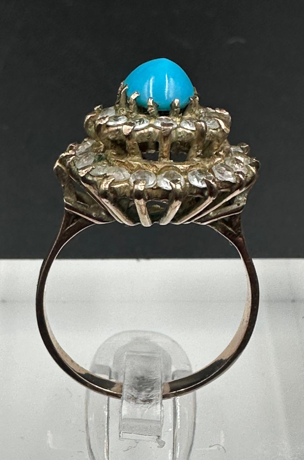 A turquoise central stone ring surrounded by clear stones on gold metal setting. - Image 3 of 3