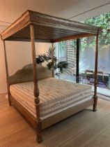 A four poster bed with carved posts and scrolling finals, the shaped bed head and canopy above