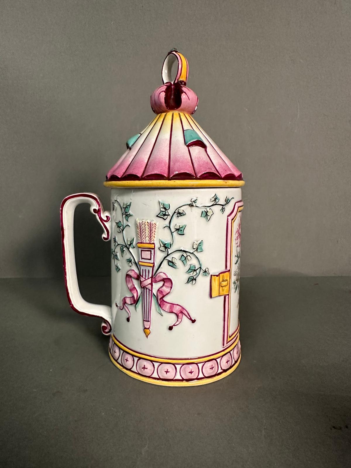A French lidded mug decorated in pinks and yellows with floral central shield