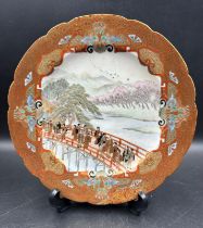 A Japanese Satsuma plate in the manner of Yabu Meizan decorated with a riverside bridge crossing