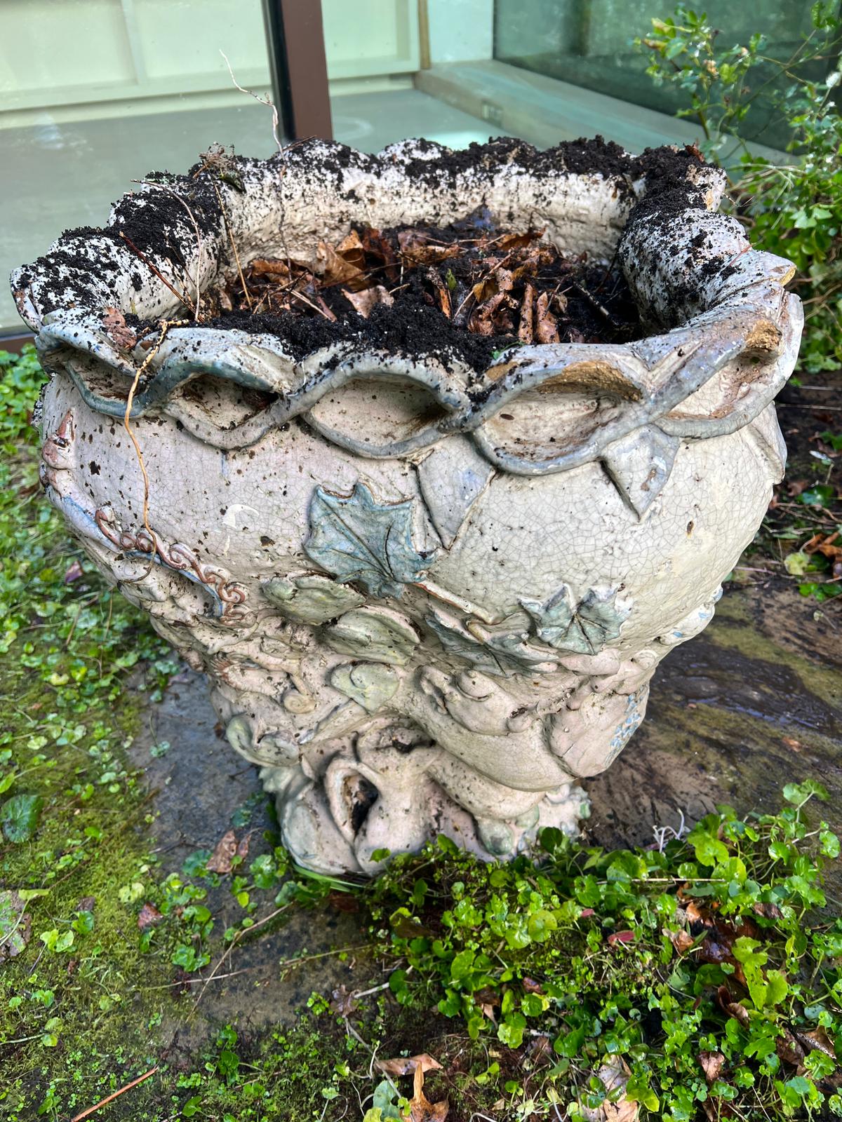 A glazed ceramic planter with platted design around the top and natural scene including a clock in a